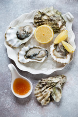 White plate with fresh opened oysters on ice and lemon, vertical shot on a beige stone surface, selective focus