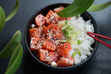 Poke bowl with salmon, white rice, green onion and sesame over black stone background, closeup, selective focus