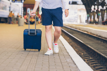 man with suitcase on wheels walking by railway station platform
