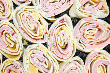 Puff pastry rolls with sausage and cheese on a baking sheet in raw form.