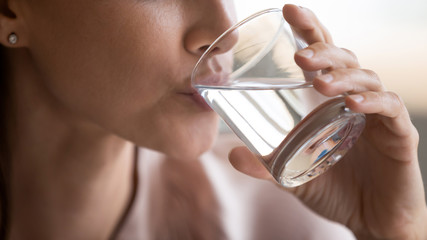 Close up beautiful thirsty woman drinking pure mineral water, holding glass in hand, attractive...