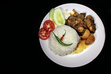 Cup of boiled rice with chicken broth on a white plate isolated on black background. Cooked rice on a white plate, chili, tomato, cucumber