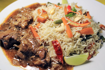 Vegetable fried rice with chili chicken on white plate isolated on yellow cloth. Top view. Chili chicken is a popular Indo-Chinese dish of chicken of Hakka Chinese heritage. 