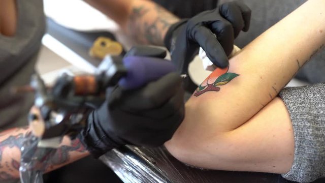 Female tattooist tattooing a peach on a woman's arm.