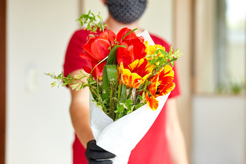 Courier, delivery man in red in medical latex gloves safely delivers online purchases a bouquet of flower during coronavirus epidemic. Stay home, safe concept. Contactless delivery service