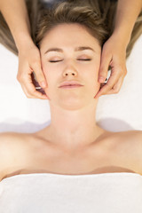 Obraz na płótnie Canvas Young blond woman receiving a head massage in a spa center.
