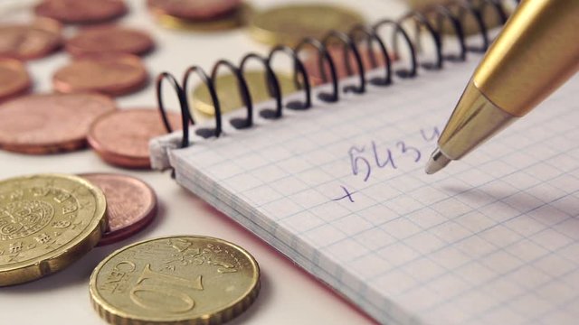 Businessman calculates financial profit and expenses in a notebook with a golden pen. Euro cent coins on the table. The concept of decline in consumption and forced savings during the coronavirus pand
