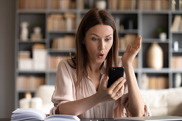 Surprised woman with open mouth looking at phone screen, reading unexpected message, shocked young...