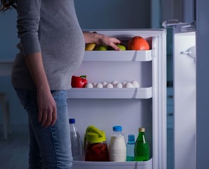 Pregnant woman near fridge looking for food and snacks at night