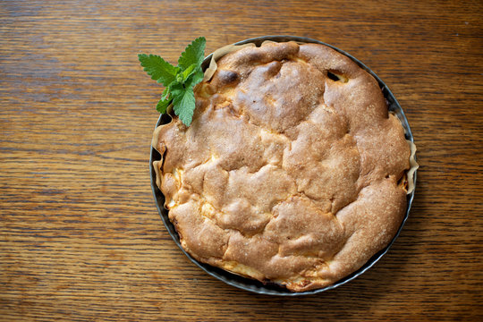 Round Home-made Apple Pie, Cobbler, Brown Betty, Apple Charlotte On Wooden Background With Mint Leaves. Rustic Style. Homemade Cake. Apple Pie Charlotte. Rustic Wooden Table Background. Rustic Style.