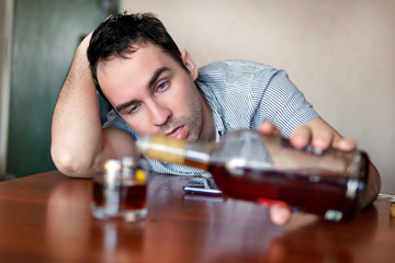 Sad sad young alcoholic sit at the table with bottle of rum. the face of a drunk man. Stupid...