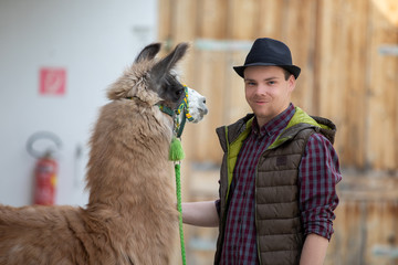 Junger Mann hält Führstrick von Lama und schaut in die Kamera © Fotoliesl