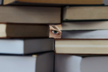 Глаз человека смотрит сквозь гору книг .  Шель между книг . 
Человек смотрит на книги 