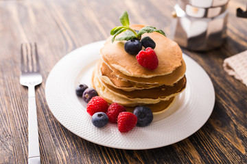 Pile of pancakes with blueberries and raspberries for breakfast on wooden table.