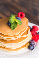 Pile of pancakes with blueberries and raspberries for breakfast on wooden table.