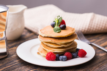 Pile of pancakes with blueberries and raspberries for breakfast on wooden table.