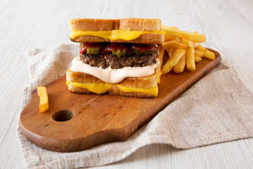 Fresh Grilled Cheese Burger with French Fries on a rustic wooden board on a white wooden background, side view. Close-up.