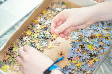 Close-up of female hands assembling a puzzle at home. The concept is home entertainment.