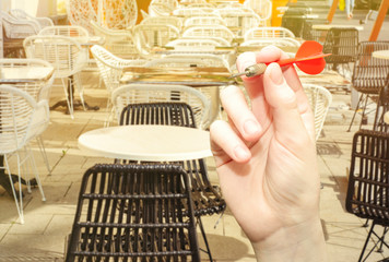 Female hand holds an arrow for darts on the background of an empty street restaurant