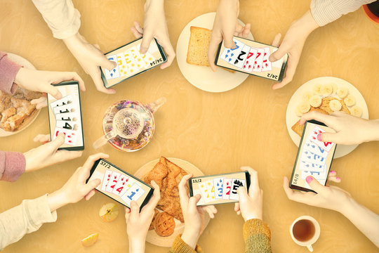 Hands of people with mobile phones playing multiplayer online games with friends over a snack table.