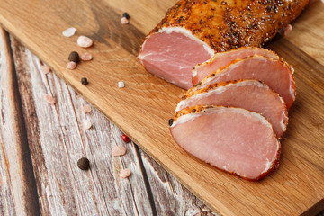 Smoked dried ham on a chopping board. Sliced smoked gammon on a wooden table with addition of fresh herbs and aromatic spices. Natural product from organic farm, produced by traditional methods