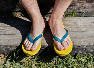 a couple of feet completely barefoot wearing two yellow and blue flip flops on a wooden step. The...