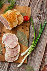 Chicken roll in grid decorated lettuce leaf isolated on wooden background. Fresh meat product whole and partly sliced. Chicken ham, and slices of tasty chicken meat. Natural product from organic farm.