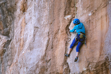 A woman in a helmet climbs a beautiful orange rock.