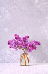 Obraz premium Beautiful blooming lilac branches in the glass jar on the table. Vertical.