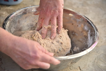 Close up of a baker kneading bread dough in a metal bowl. 
Handmade bread dough in a stainless steel bowl.