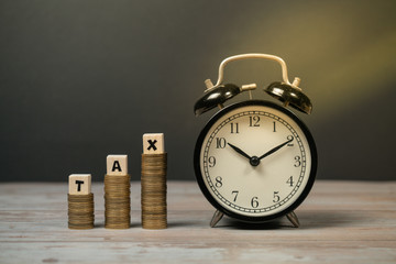 Time to pay TAX concept. TAX alphabet with stack of coin and vintage alarm clock over sun flare in dark background, business and financial concept idea.