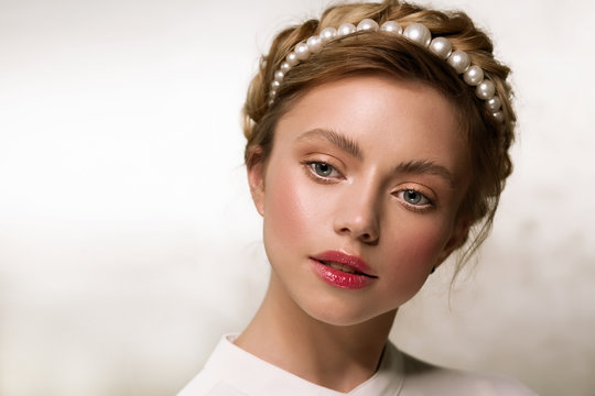 Portrait of a beautiful young woman with a hairpin or hoop of round beads in her hair. Bride. Gentle natural make-up. She looks thoughtfully down.