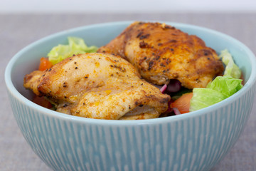 Chicken breast in a bowl with tomato, lettuce, onion, cucumber, and pepper in a vinaigrette.  On a grey marl tablecloth