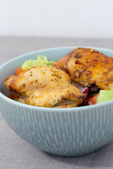 Chicken breast in a bowl with tomato, lettuce, onion, cucumber, and pepper in a vinaigrette.  On a grey marl tablecloth