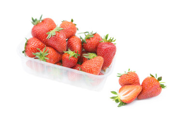 Fresh organic ripe strawberries in a plastic tray and two and a half near rotated isolated on white background