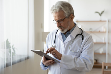 Senior male doctor using digital tablet computer tech providing online healthcare telemedicine...