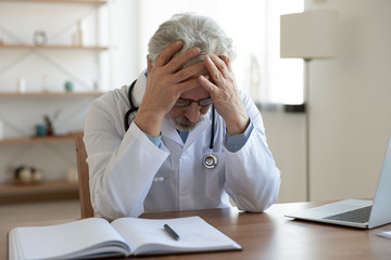 Tired depressed old male doctor feels desperate thinking of medical problem feels burnout at work....