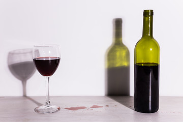 Bottle with wine and glass, red puddle of wine on the table. Cleaning after party concept.