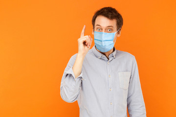 I have idea. Portrait of excited young worker man with surgical medical mask standing with surprised face and has a idea. indoor studio shot isolated on orange background.