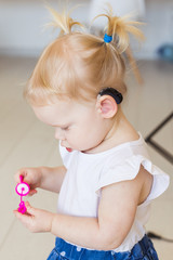 Fototapeta premium Hearing aid in baby girl's ear. Toddler child wearing a hearing aid at home. Disabled child, disability and deafness concept.