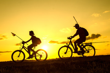 Fototapeta na wymiar Father and son returning from fishing in the evening, silhouettes of people on bicycles in nature