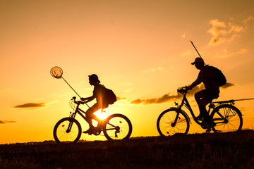Fototapeta premium Father and son returning from fishing in the evening, silhouettes of people on bicycles in nature