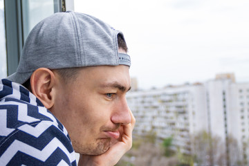 Young sadness caucasian man in looking out to home balcony terrace who s quarantined in his apartment due to coronavirus covid19 pandemic.