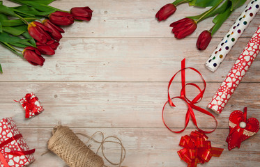Flower composition. A bouquet of spring red tulips, gift boxes, wrapping paper, ribbons and bows on a light wooden background. Free space.