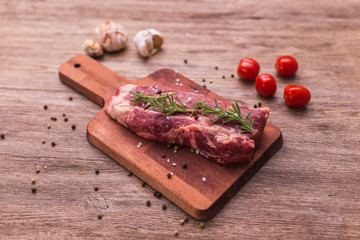 Raw meat. A large piece of beef chop on a wooden cutting board with rosemary and spices.