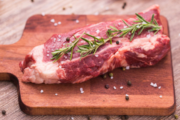 Raw meat. A large piece of beef chop on a wooden cutting board with rosemary and spices.