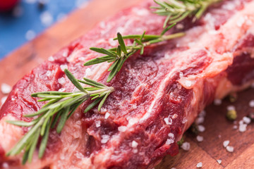Raw beef fillet steaks with herbs and spices on wooden background, close-up.