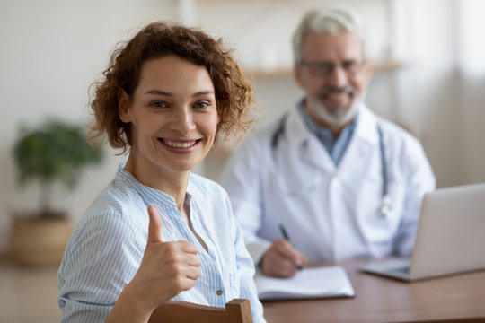 Satisfied healthy smiling young adult woman patient looking at camera sitting at old doctor consultation showing thumbs up recommend good quality women healthcare medical services concept. Portrait.