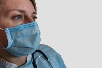 Doctor or nurse in medical uniform, mask and stethoscope. Close-up portrait of white woman not looking into the camera in half face position on gray isolated background with copy space