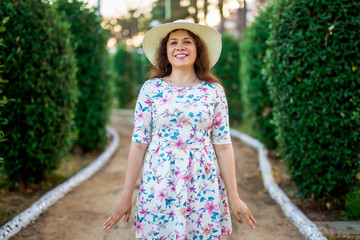 Portrait of pretty woman wearing white dress and straw hat in sunny warm weather day. Walking at summer park.